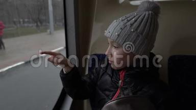 <strong>一个</strong>戴着帽子的可爱<strong>小</strong>女孩坐在公共汽车后座的<strong>玻璃</strong>上画画。从窗口经过的人